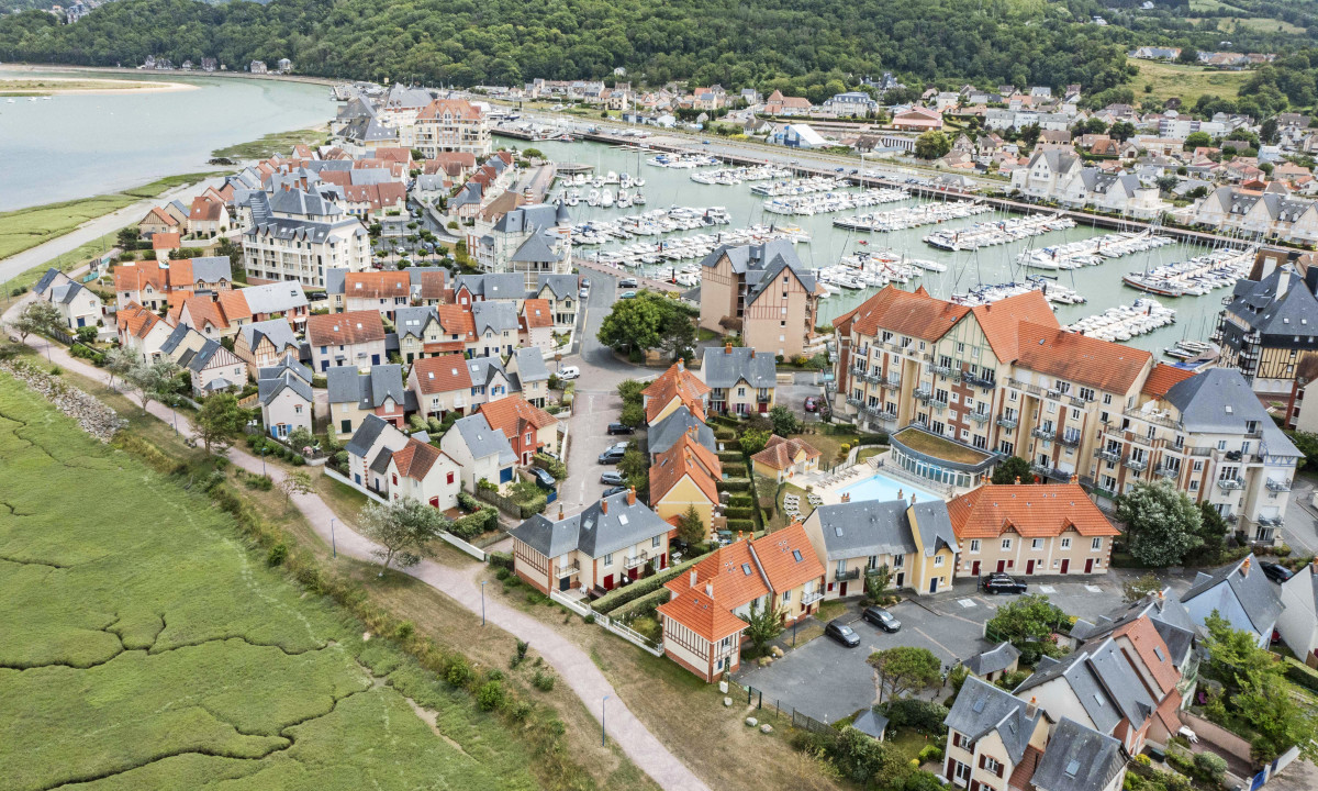 Colorful houses and buildings surround a marina full of boats, with lush green hills and winding river in the background at Port Guillaume