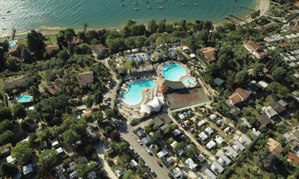 Aerial view of a campground with pools and a tennis court near a lake, surrounded by trees and cabins at Europa Silvella