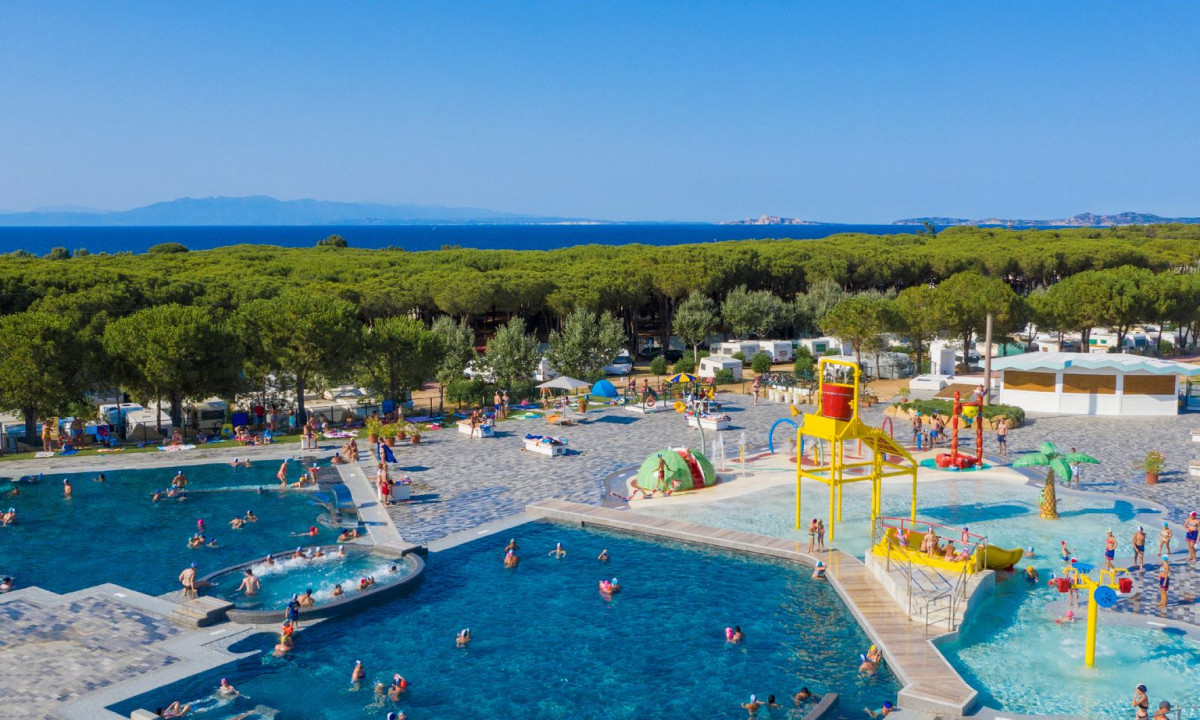 People swimming and playing in multiple outdoor pools and water play areas with trees and ocean in the background at Baia Blu La Tortuga