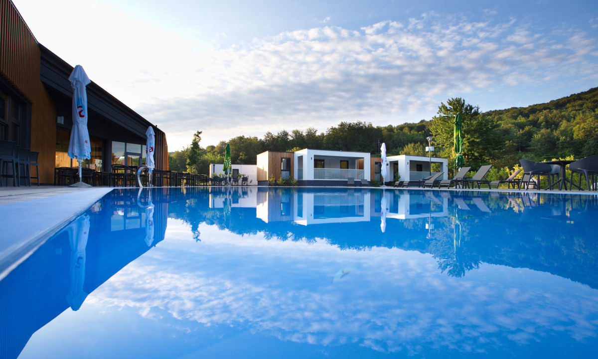 Reflection of buildings and umbrellas in a clear swimming pool surrounded by lush greenery at Plitvice