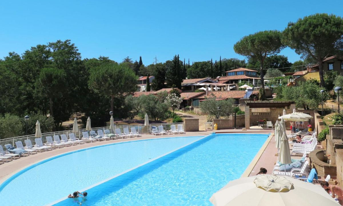 Pool with swimmers, surrounded by lounge chairs and umbrellas, nestled in a lush hillside setting at Centro Vacanze Il Borgo