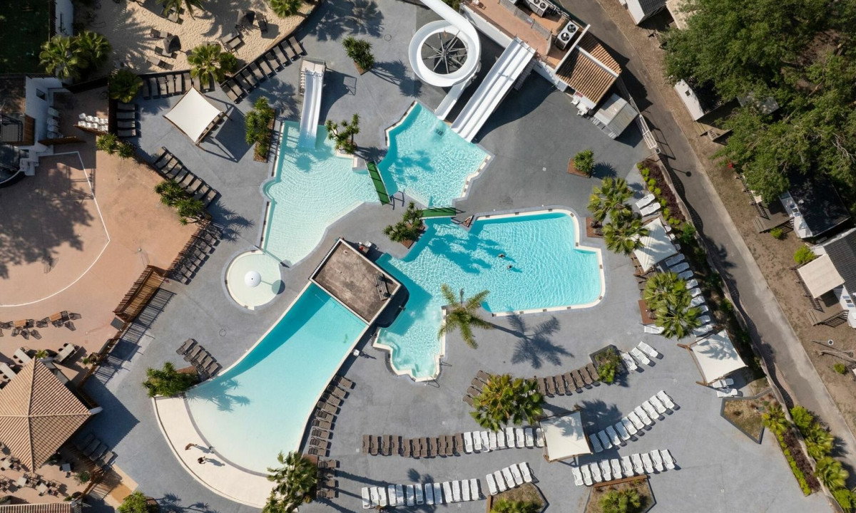 Swimming pools with slides surrounded by lounge chairs and palm trees at Les Vagues