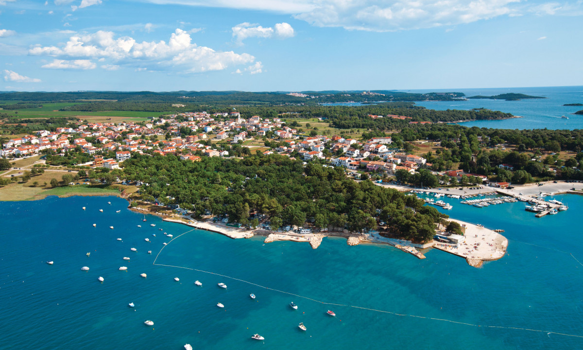 Boats floating in a crystal-clear bay near a small coastal town surrounded by lush green trees and clustered houses at Puntica