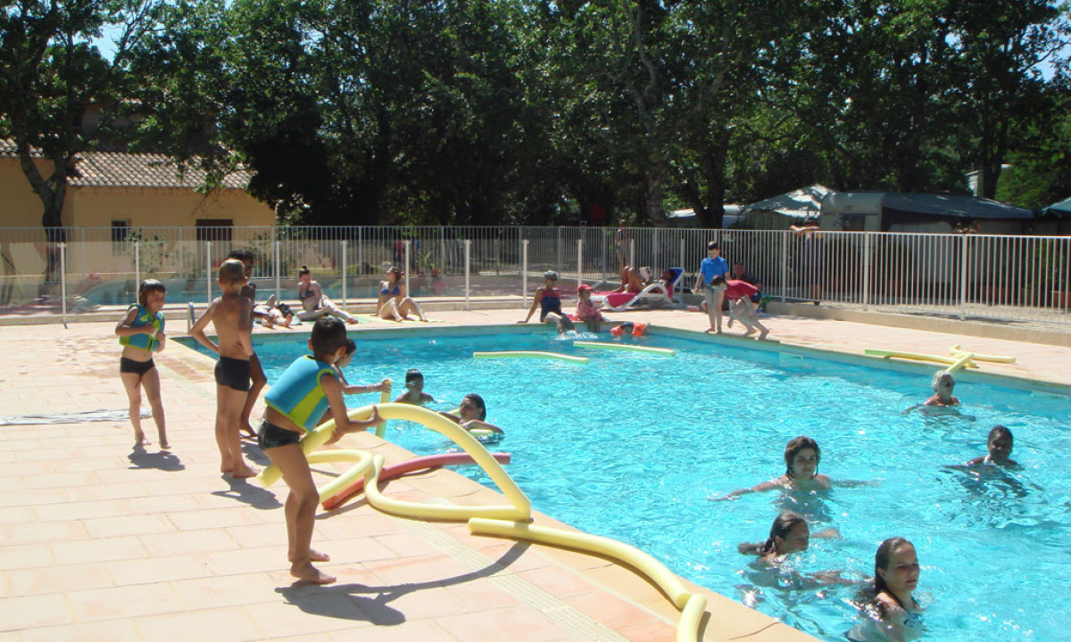Children playing in a swimming pool while others relax poolside, surrounded by trees and camping area infrastructure at La Buissière