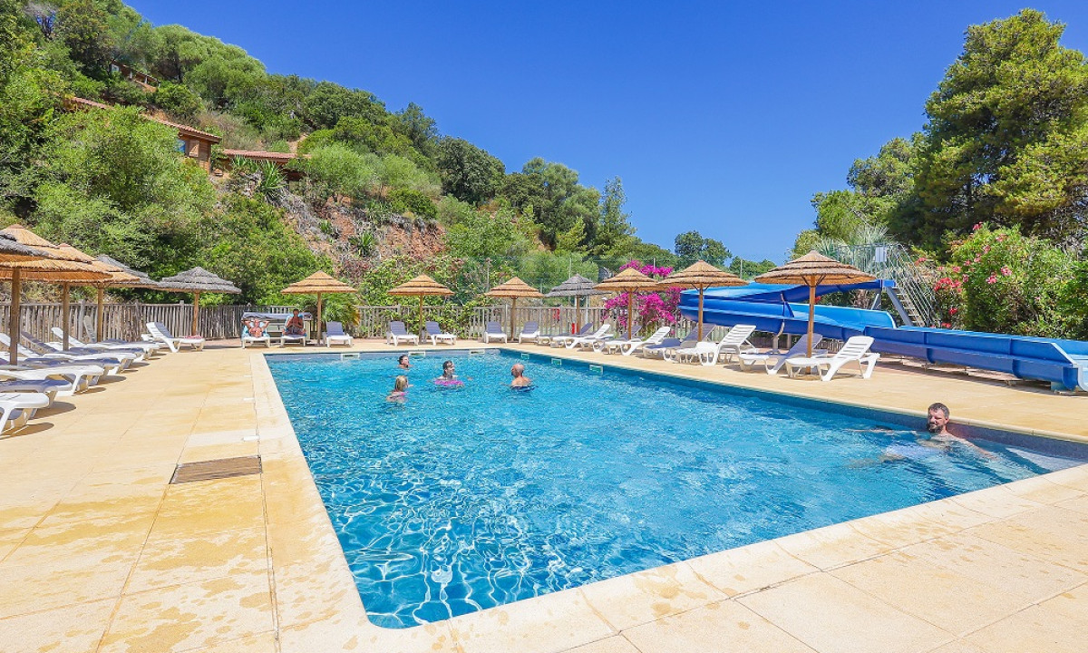 People swimming in a pool surrounded by lounge chairs and umbrellas, with lush hills and clear blue skies at Torraccia