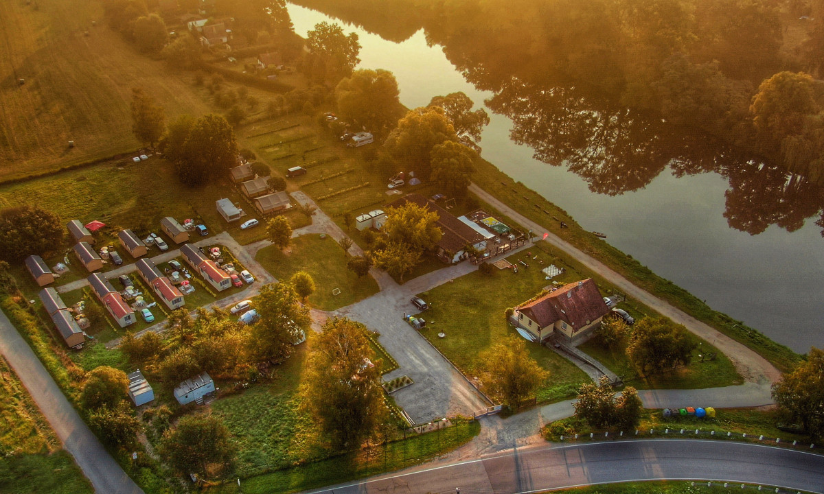 Aerial view of a campsite with cabins near a river, surrounded by trees and grassy areas at Prima